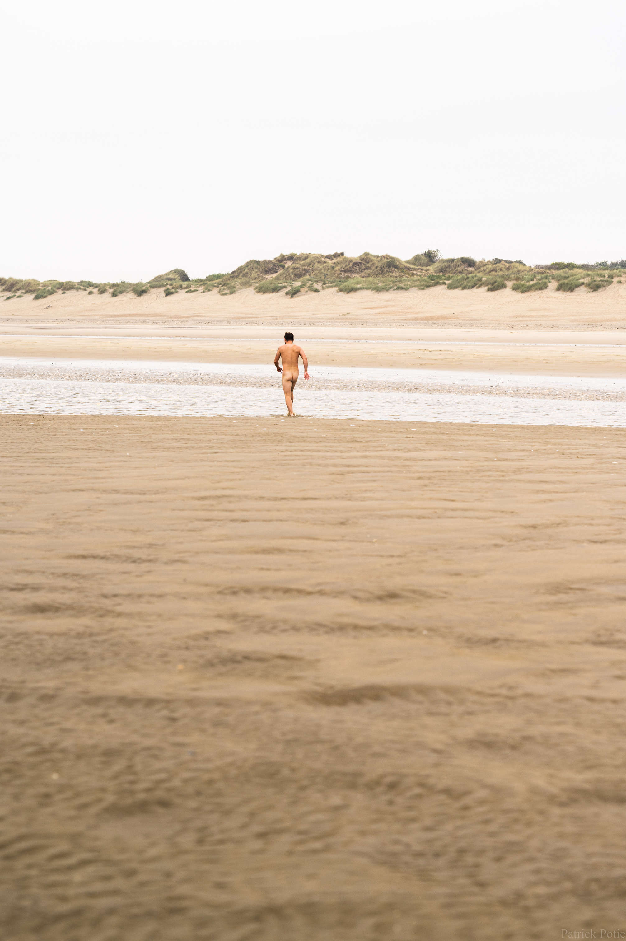 homme posant nu sur le sable, dans la mer et dans les dunes