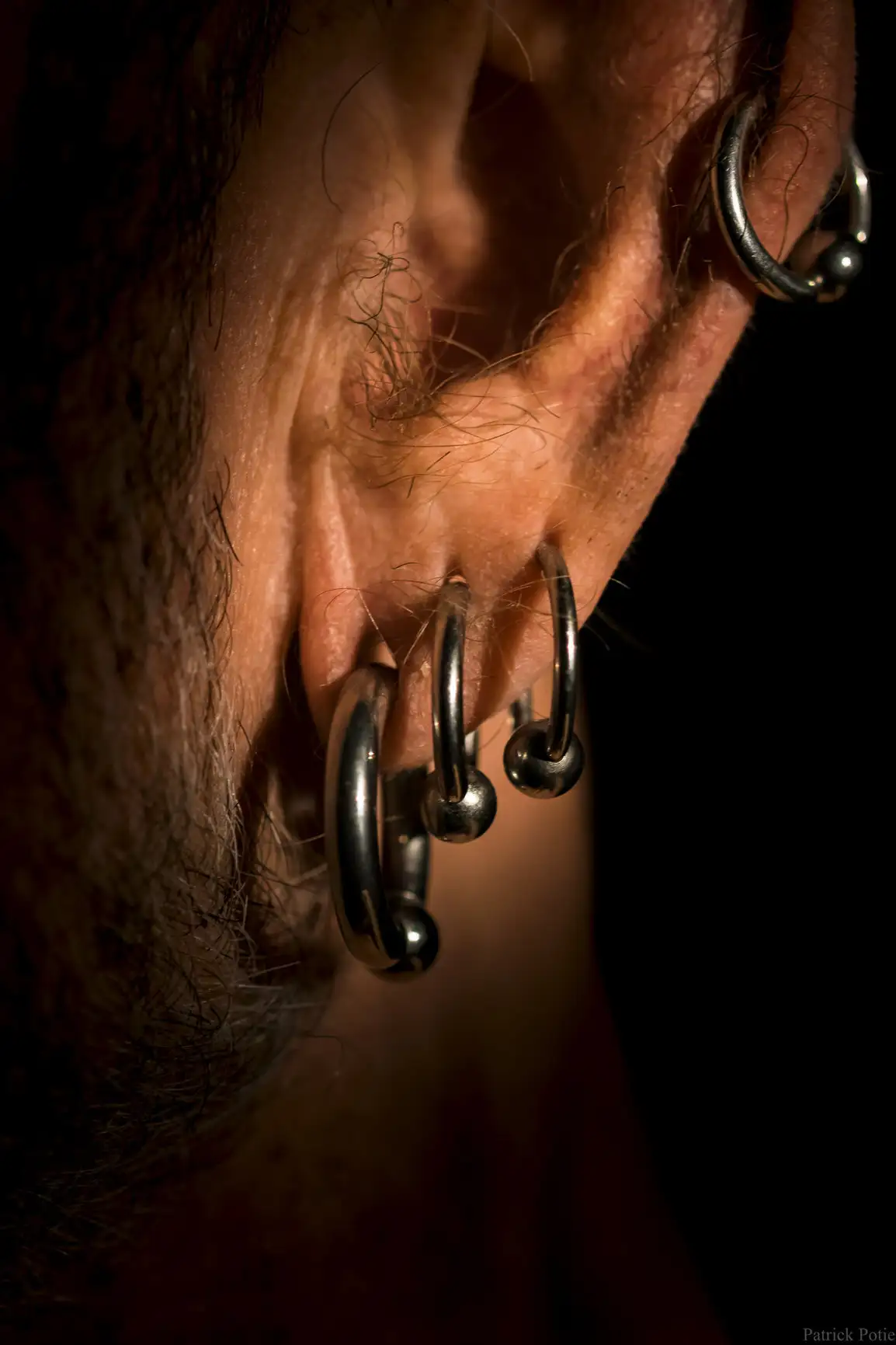 Oreille d'un homme âgé présentant plusieurs piercings à anneaux métalliques à billes captives.