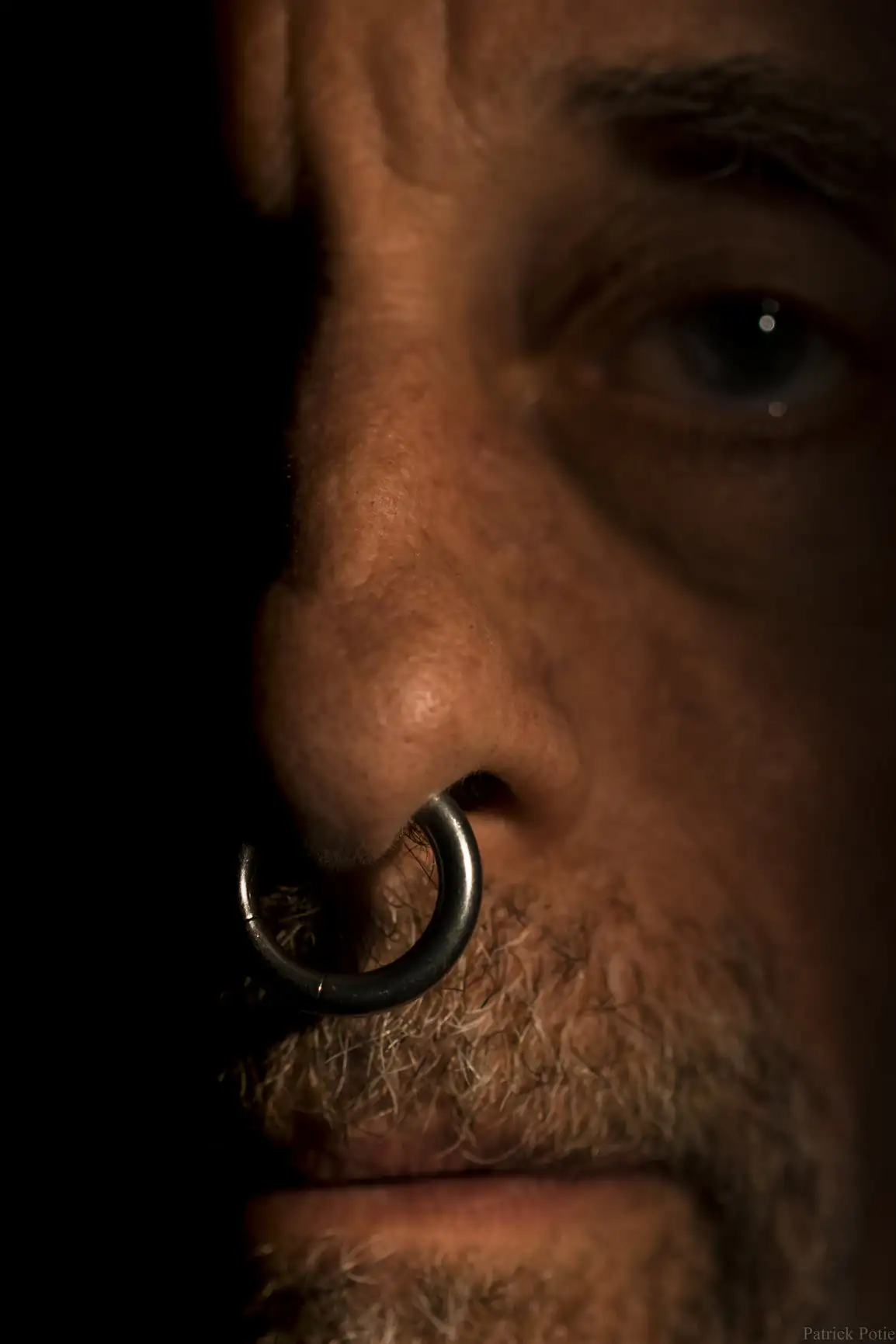 Un homme mûr, le septum percé avec une barbe, regarde la caméra.