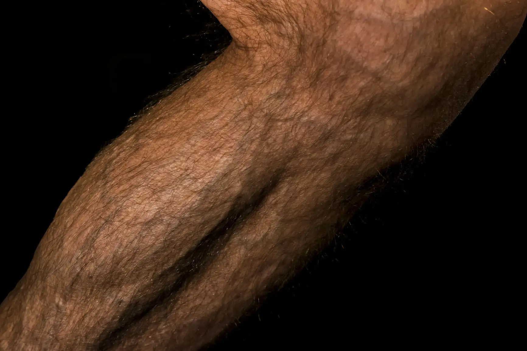 Mollet masculin contracté, veines apparentes et poils visibles, témoignant de sa force et de sa forme physique.