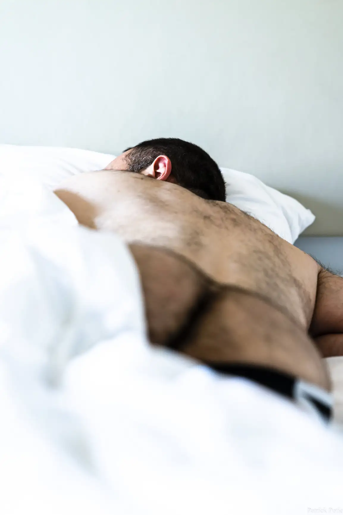 Dos d'un homme poilu qui dort sur le côté sous une couette blanche