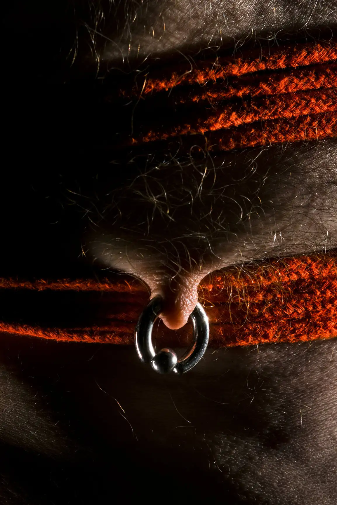 sein masculin avec piercing et corde rouge sous une lumière tamisée