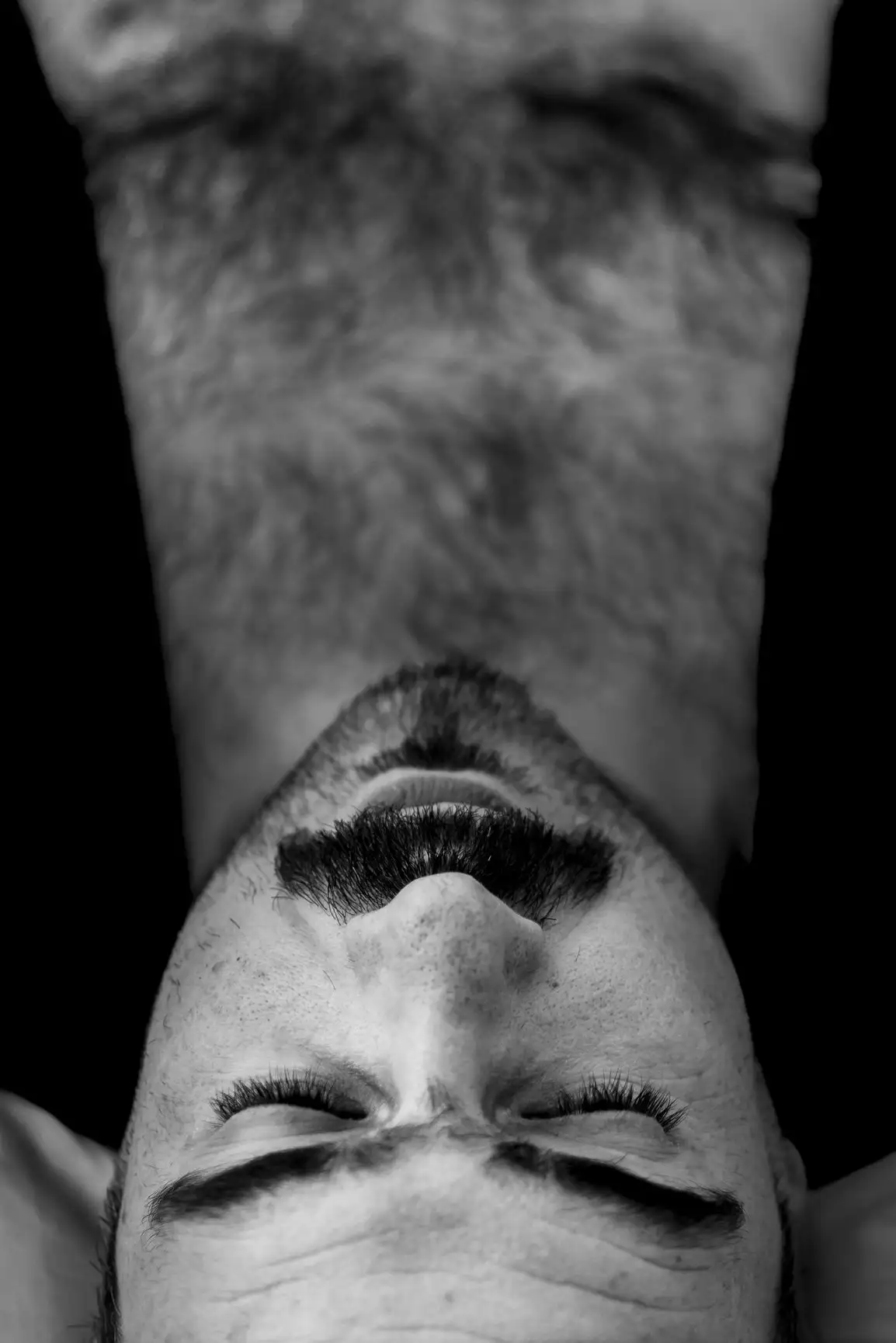 Un homme à moustache et barbe ferme les yeux, offrant une perspective inversée et dramatique