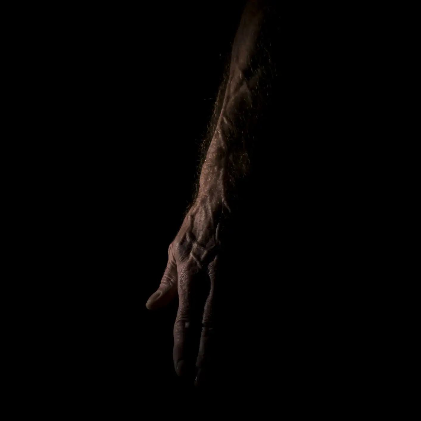 Un bras et une main âgés et ridés se détachent sur un fond sombre