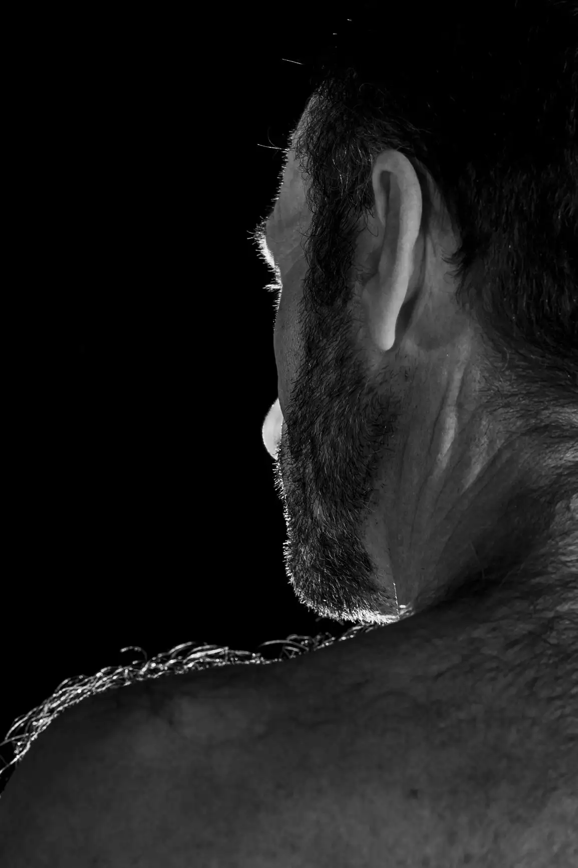Homme barbu à l'épaule poilue sur fond noir, éclairé par un éclairage indirect