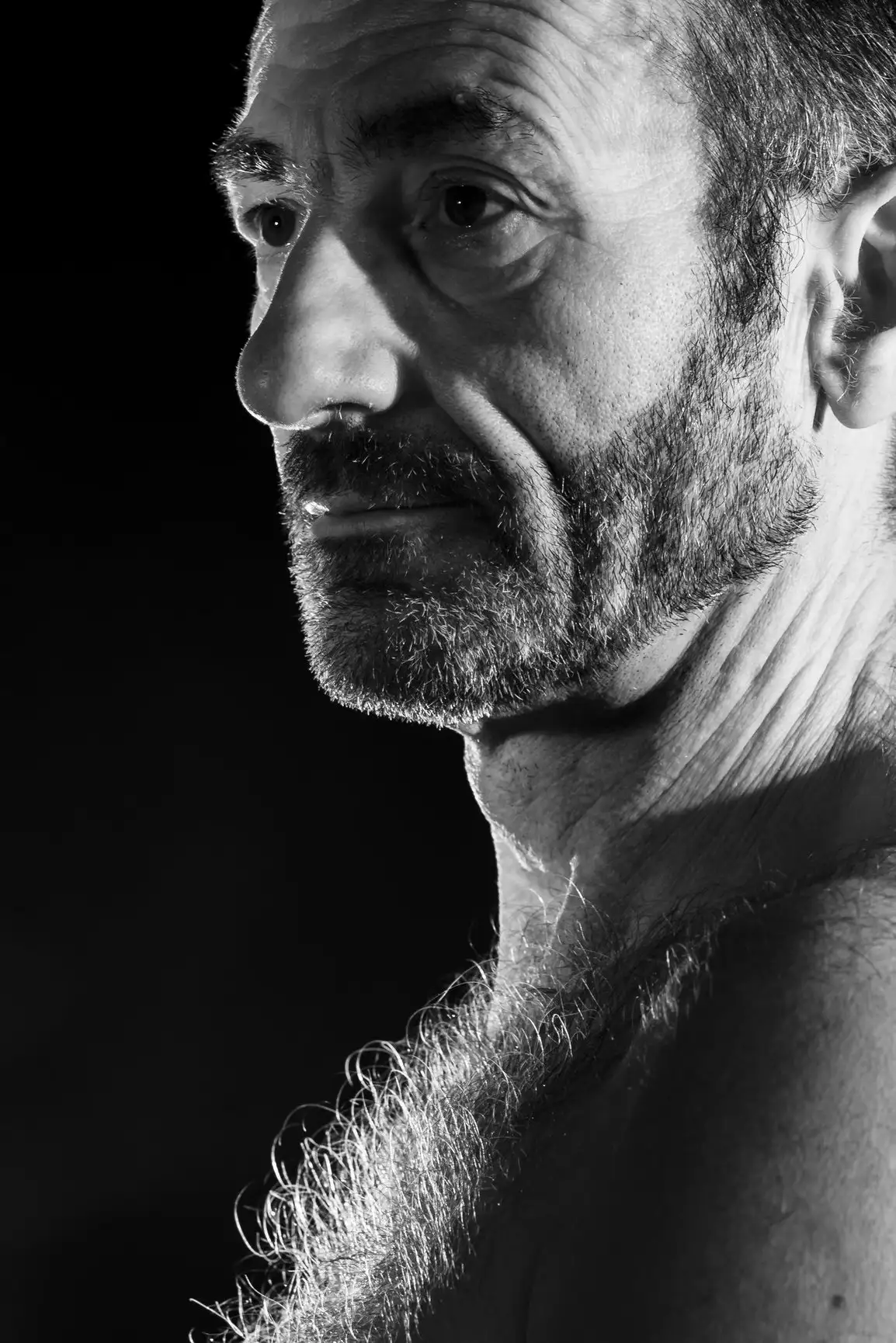 Un homme mûr, barbu et poilu sur la poitrine, regarde droit devant lui, plongé dans une profonde contemplation.