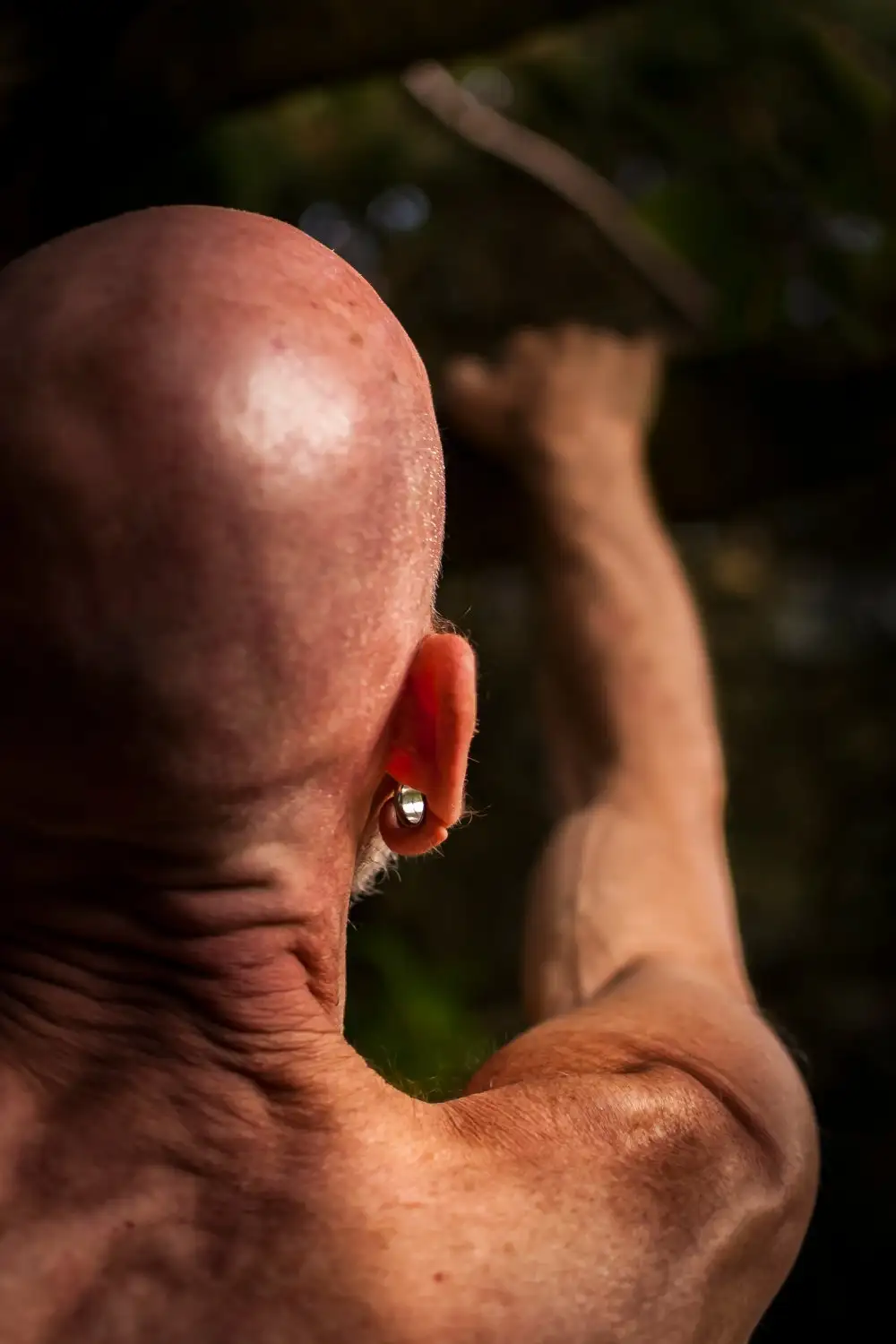 Un homme chauve portant une boucle d'oreille, révélant une peau et des muscles vieillis sous la lumière du soleil.
