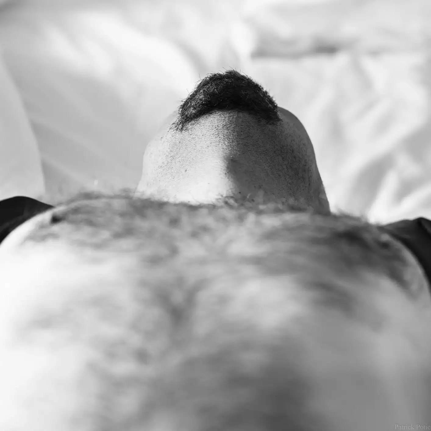 Un homme se détend au lit, dévoilant son menton et son torse velu sous un angle original.